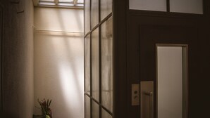 A narrow hallway with a potted plant, a door with a light switch, and a window with blinds. - Hotel Montana (Geneva)