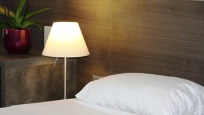 A neatly made bed with white linens, a bedside lamp, and a potted plant on a wooden nightstand. - Hotel Montana (Geneva)