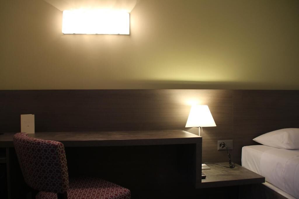 A hotel room with a desk, chair, bedside lamp, and a bed.