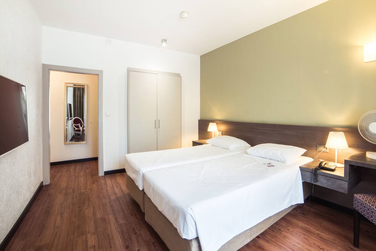 A hotel room with a large bed, two bedside tables with lamps, a wardrobe, and a mirror.