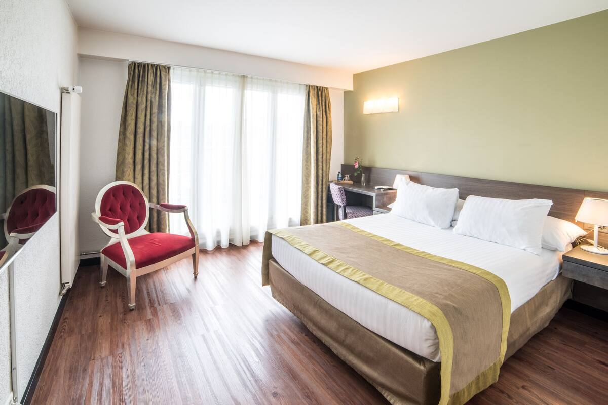 A hotel room with a large bed, a desk, a chair, and a mirror.