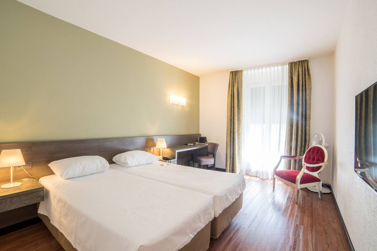 A hotel room with a large bed, bedside tables, a desk, a chair, and a TV.