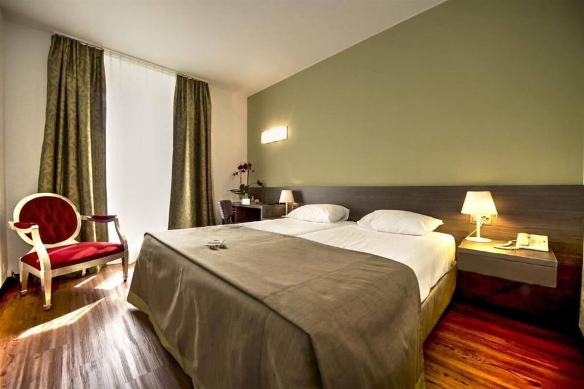 A hotel room with a bed, a chair, a nightstand, and a lamp.