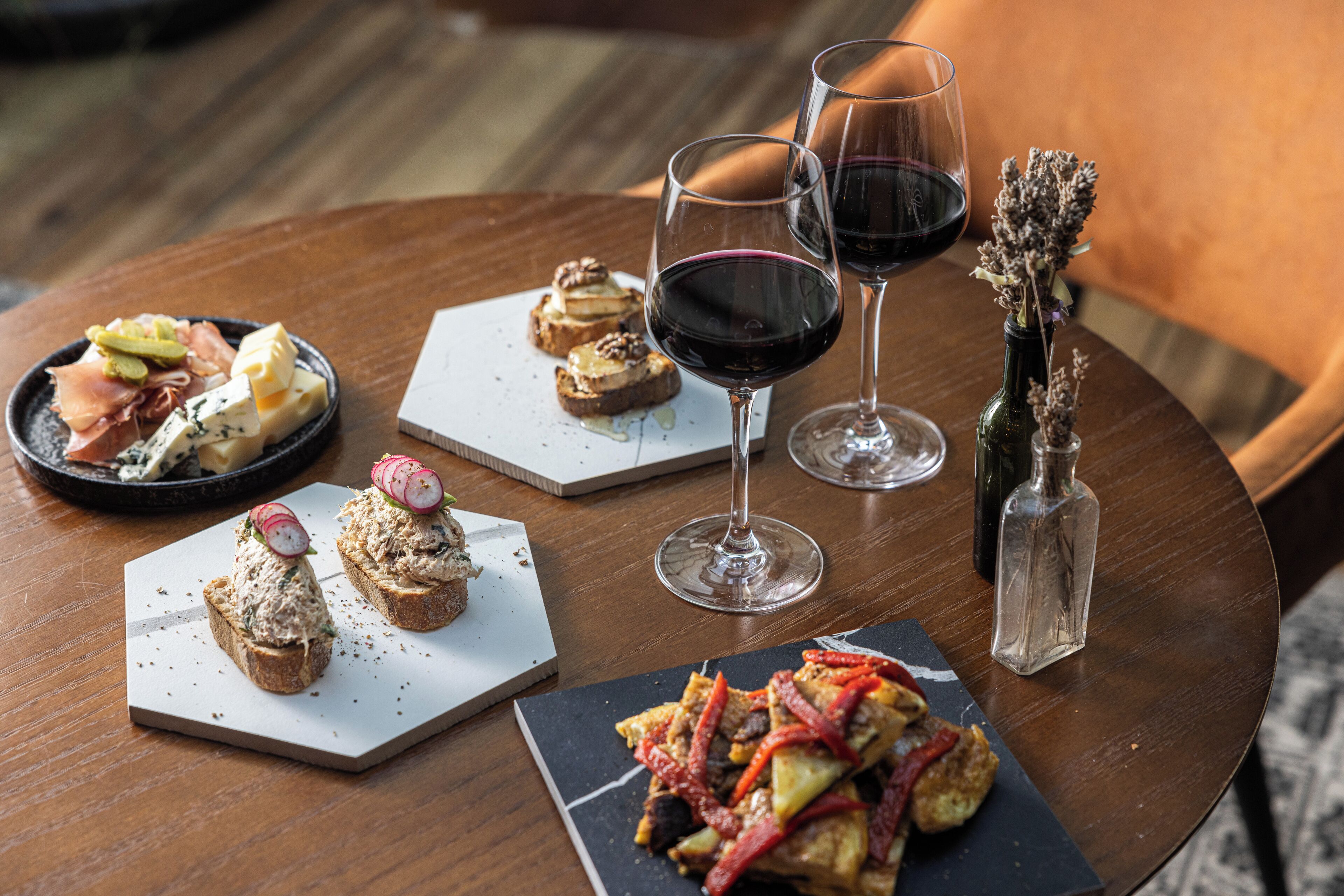 A round wooden table with various food items and wine glasses.