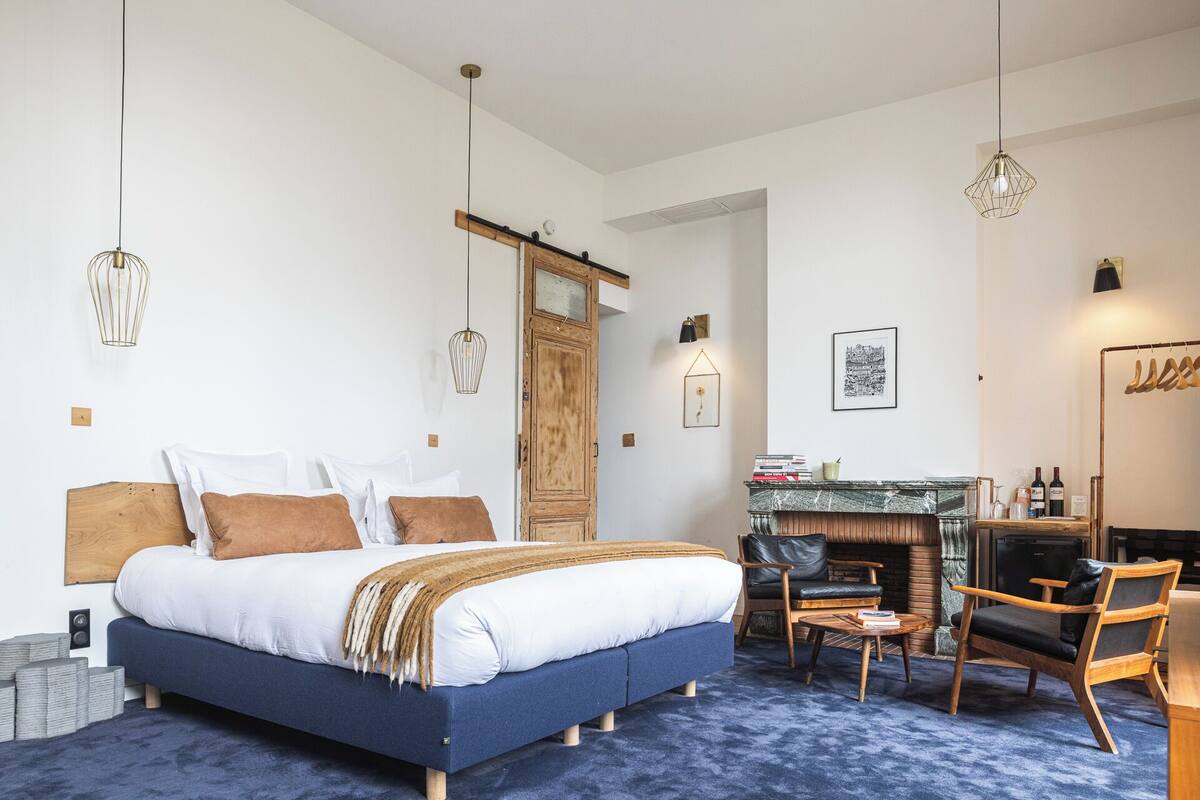 A modern bedroom with a large bed, a wooden wardrobe, a fireplace, and a seating area with a coffee table.