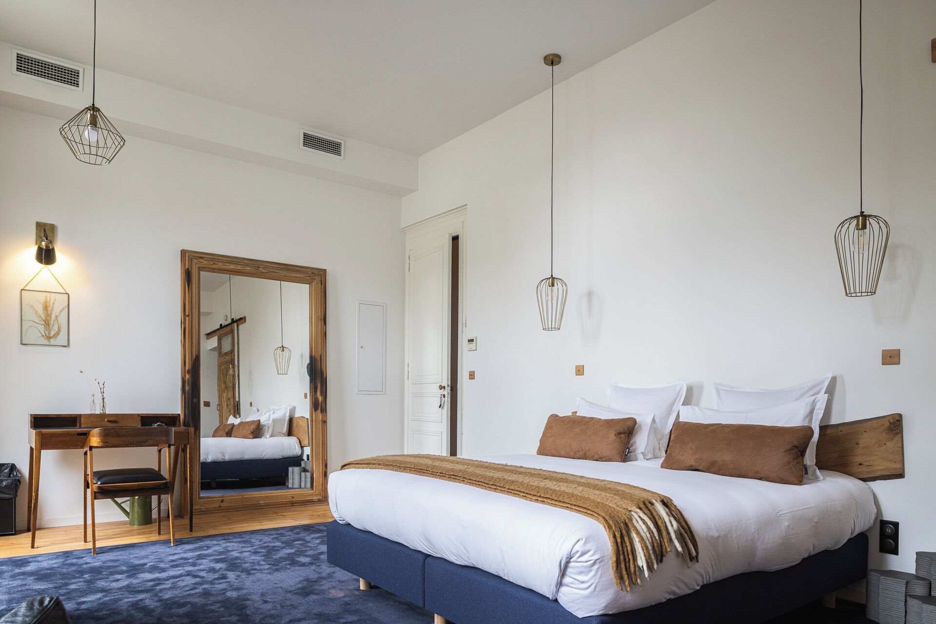 Un dormitorio con una cama grande, un escritorio de madera, un espejo y lámparas colgantes.