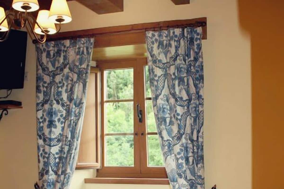 Ein Schlafzimmer mit Holzboden, einem Bett mit blumigem Überwurf und Vorhängen in Blau und Weiß.