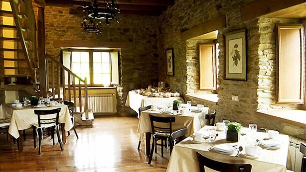 A dining area with multiple tables set for meals, stone walls, and a staircase. - Casa Berbesa (Castropol)