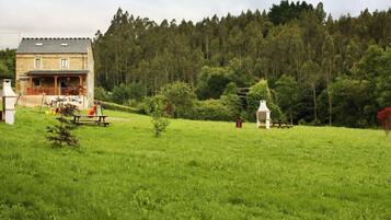 Surrounded by a lush green field and a dense forest, this serene stone house offers a peaceful retreat.