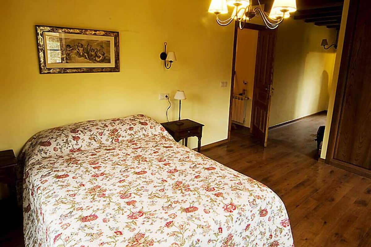 Ein Schlafzimmer mit einem blumigen Bettüberwurf, einem Chandelier, einem gerahmten Bild und einer Holztür.