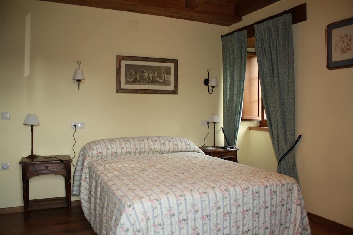 Ein Schlafzimmer mit einem Bett, zwei Nachttischen, einem Fenster mit Vorhängen und einem gerahmten Bild an der Wand.