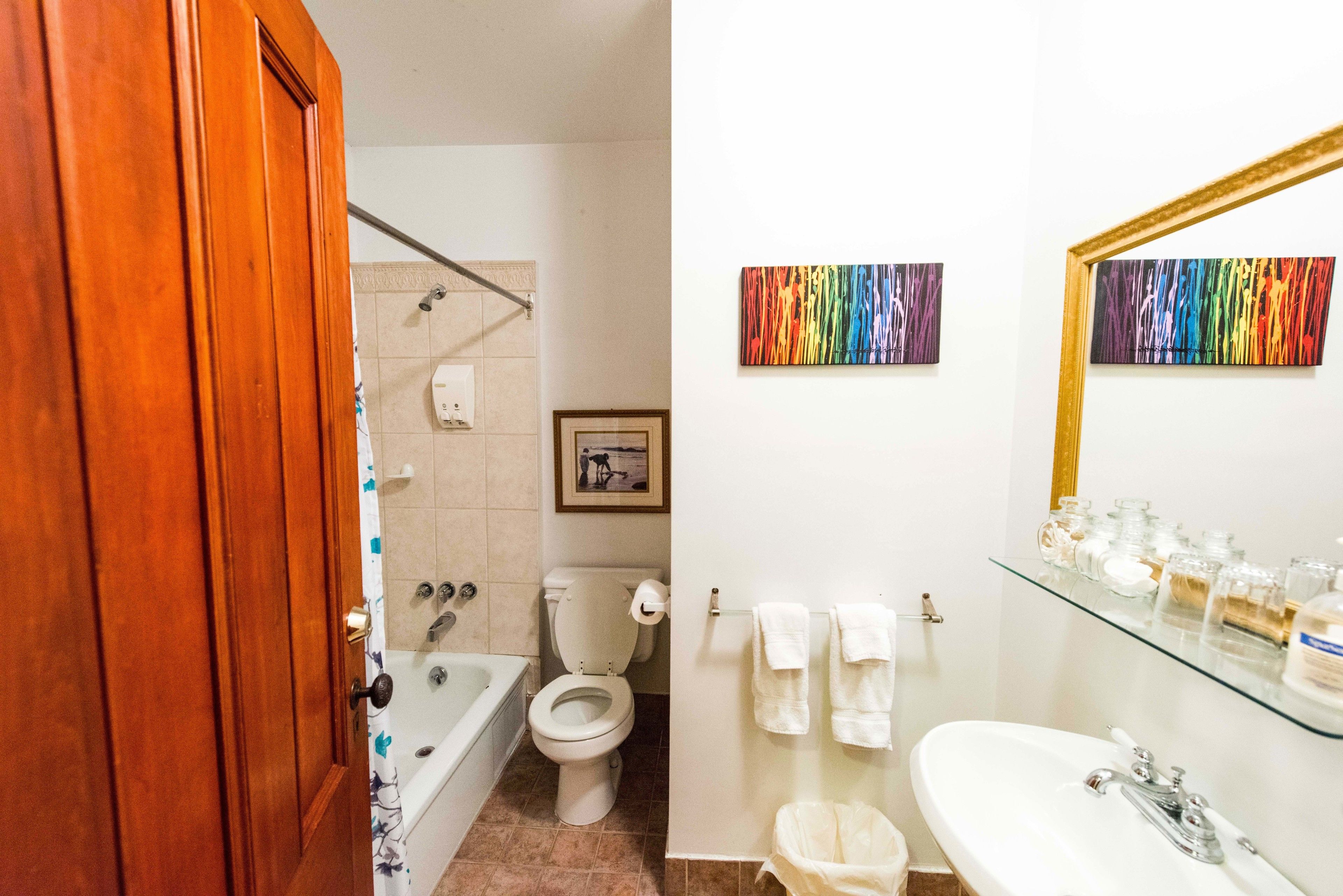 A bathroom with a bathtub, toilet, and sink. There are towels hanging on the wall and a framed picture above the toilet.