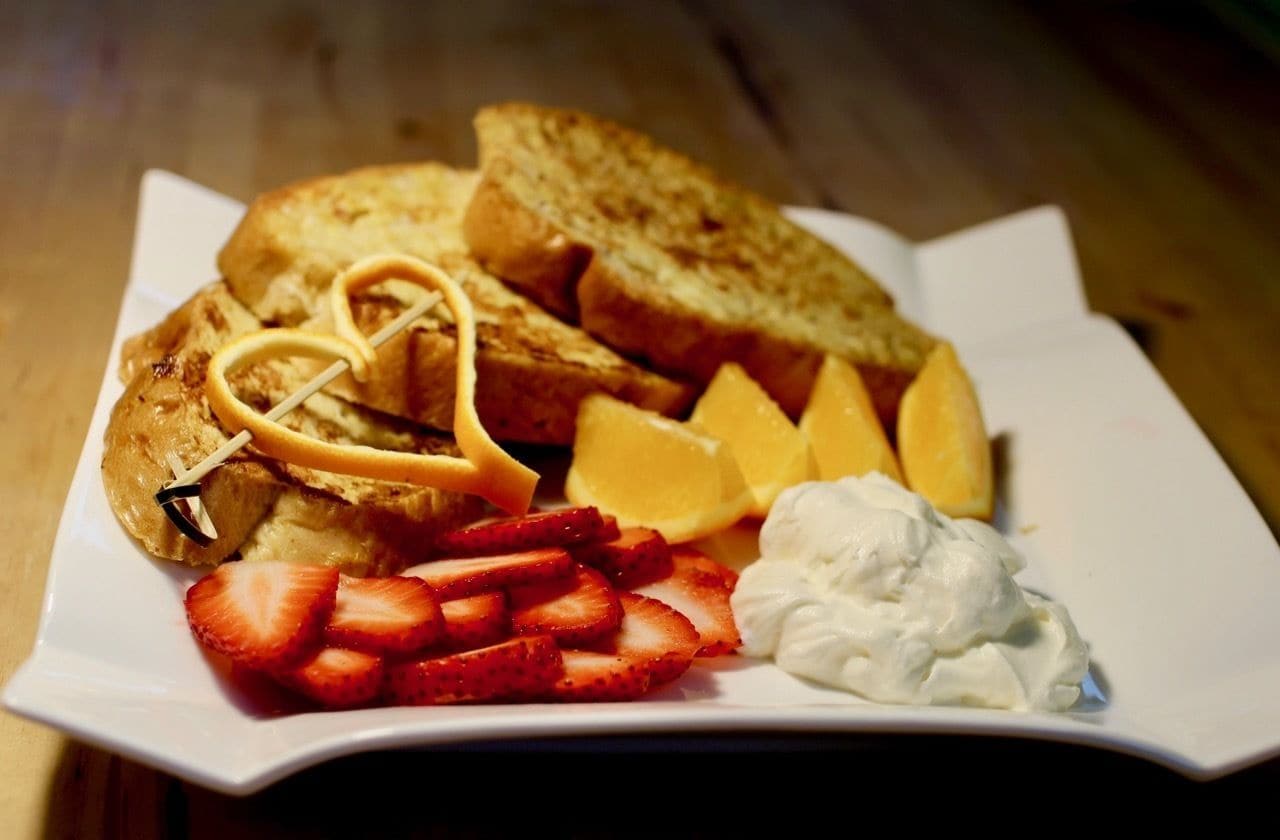 A plate with toast, strawberries, whipped cream, and a piece of fruit.