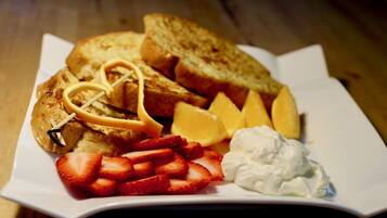 A plate with toast, strawberries, whipped cream, and a piece of fruit.