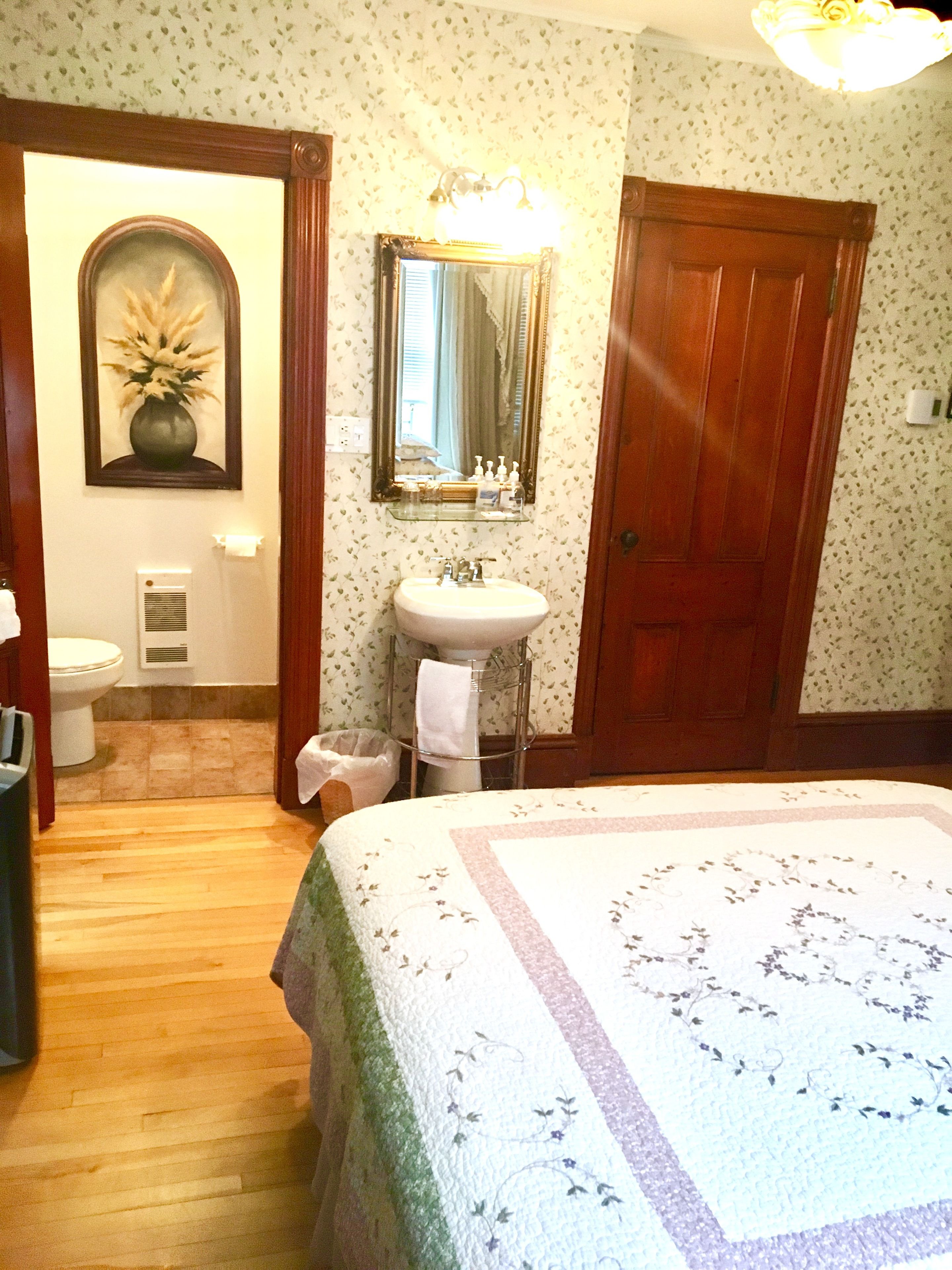 A bedroom with a large bed, a wooden door, a mirror, a sink, and a toilet.