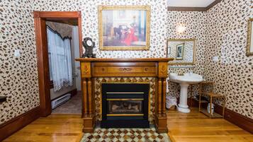 A room with patterned wallpaper, a fireplace, a painting above it, and a mirror on the wall.