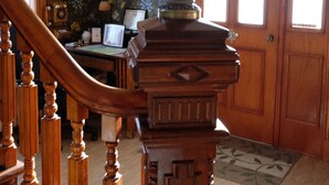Una escalera de madera con una lámpara decorativa en la parte superior, un escritorio con una computadora y un estampado de papel tapiz floral.
