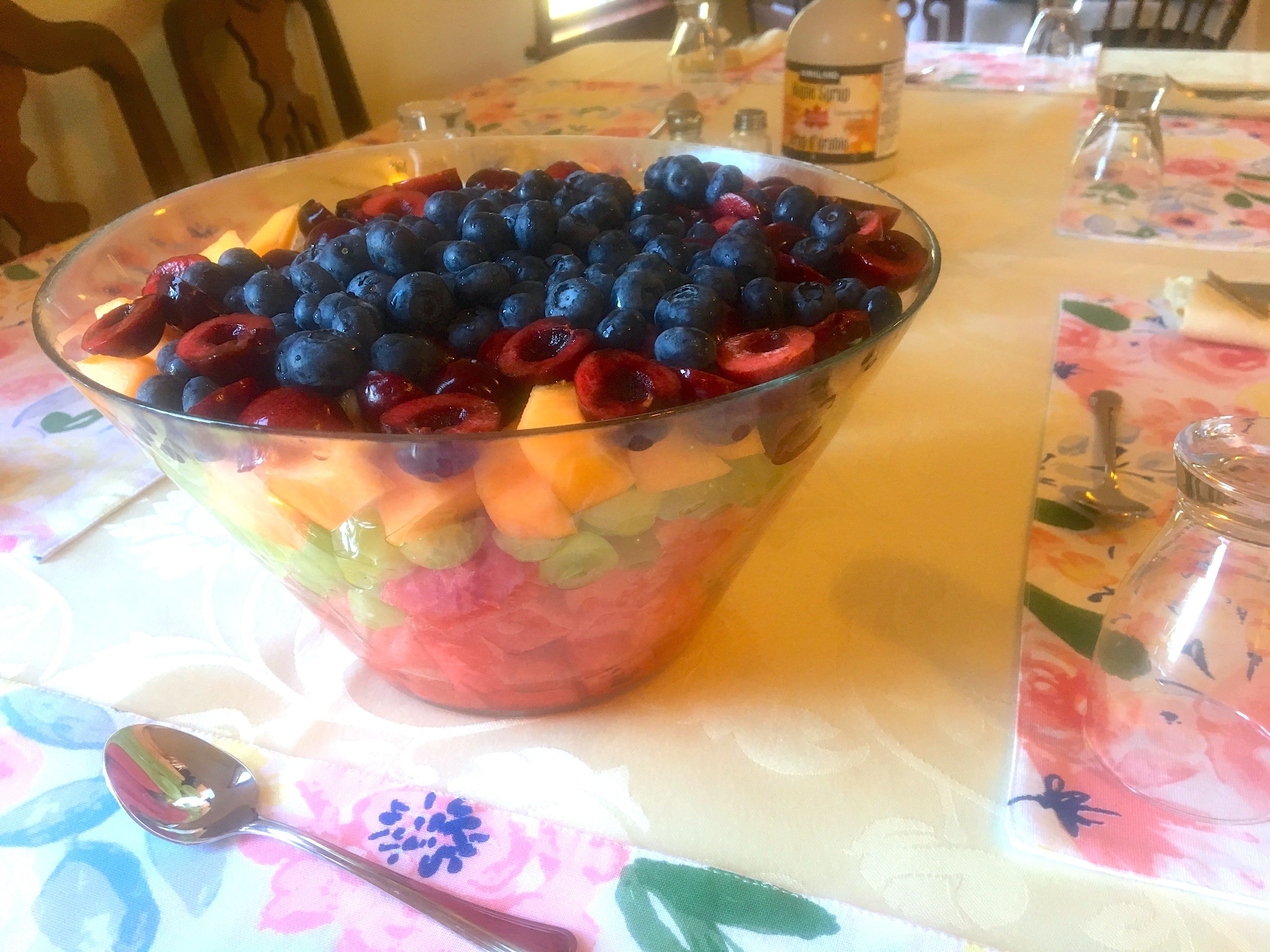 Ensalada de frutas en un bol de vidrio sobre una mesa con mantel floreado.
