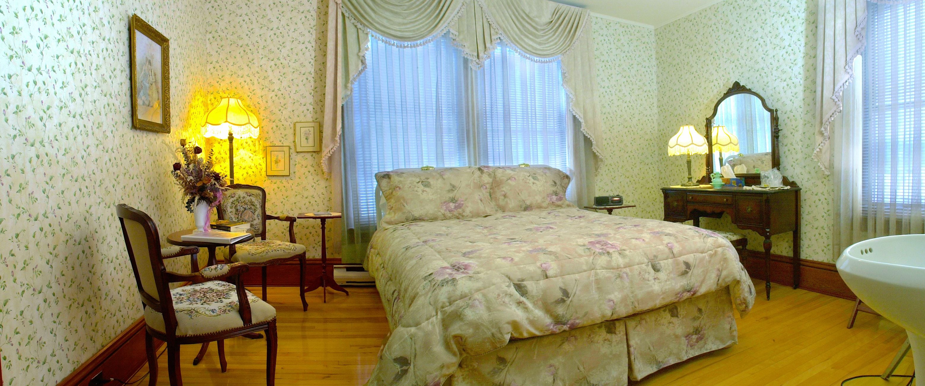 Un dormitorio con una colcha estampada, un aparador de madera, un tocador con espejo y una silla.