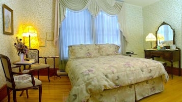 Un dormitorio con una colcha estampada, un aparador de madera, un tocador con espejo y una silla.