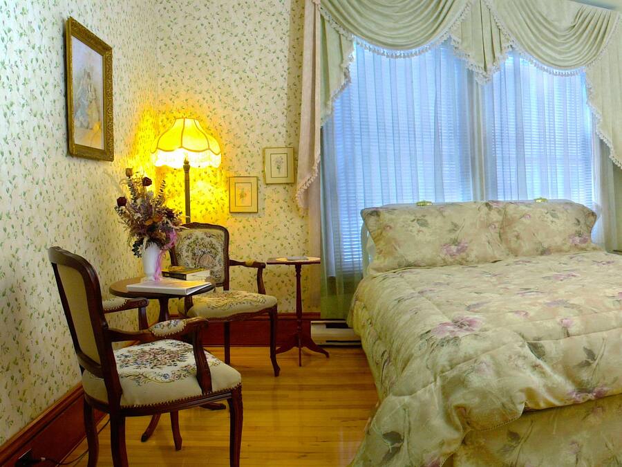 Un dormitorio con una colcha estampada, un aparador de madera, un tocador con espejo y una silla.