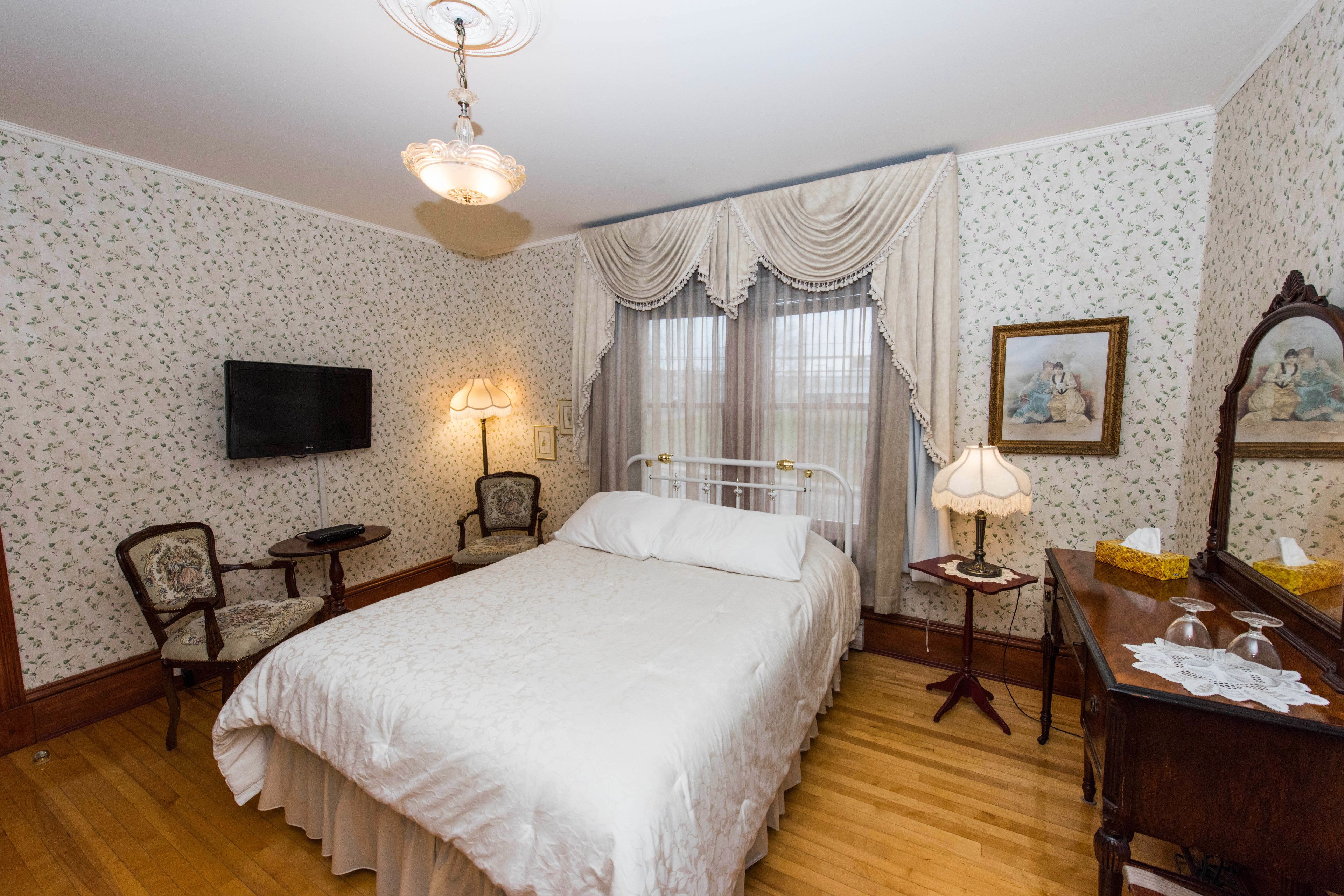 A bedroom with a bed, a television, a chair, a bedside table, and a lamp.