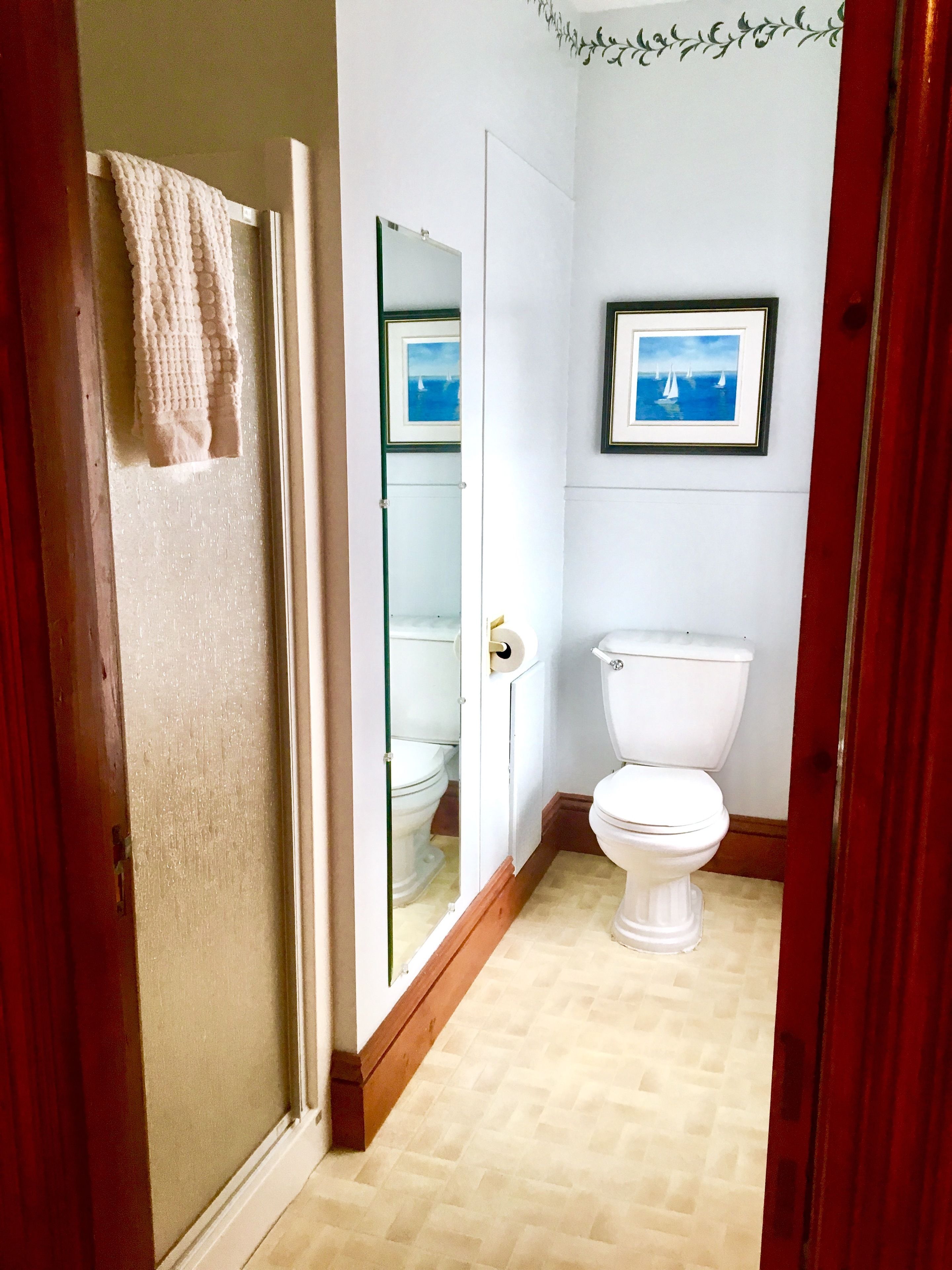 Un bagno con il water, un quadro appeso alla parete e un asciugamano appeso alla porta.