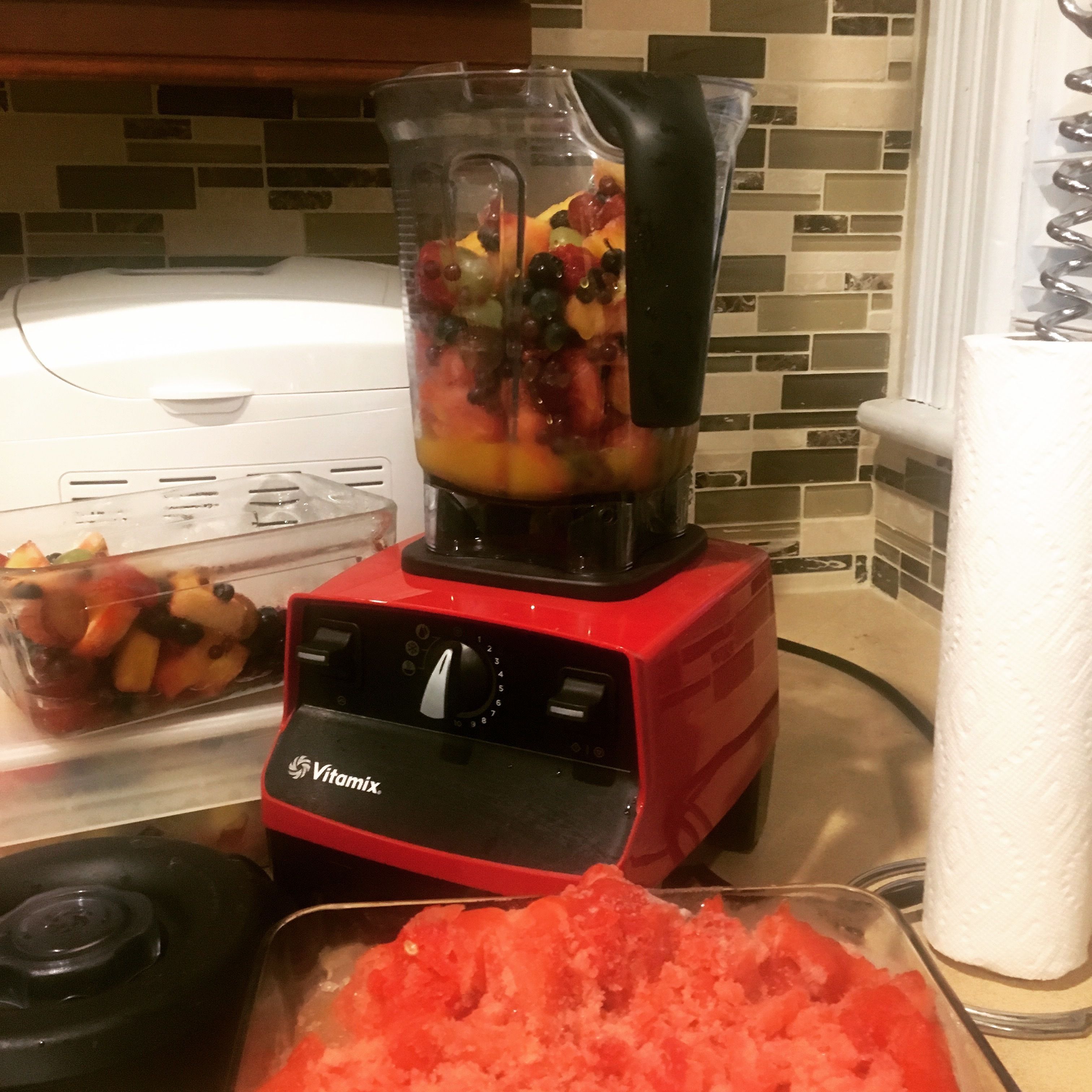 Punainen Vitamix-tehosekoitin, joka on täynnä hedelmiä ja vihanneksia, keittiön työtasolla.