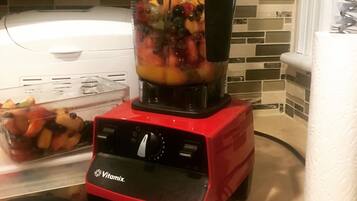 Punainen Vitamix-tehosekoitin, joka on täynnä hedelmiä ja vihanneksia, keittiön työtasolla.