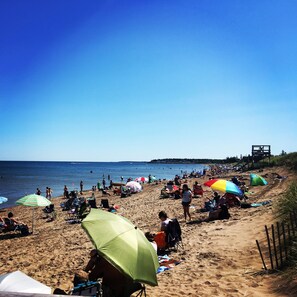 A beach with people sunbathing and swimming, umbrellas, and beach chairs. - Le Griffon B&B (Shediac)