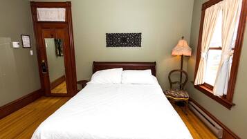 A neatly made bed with white linens, a wooden headboard, a wall-mounted decorative piece, a chair with a cushion, and a window with curtains.