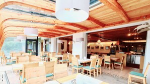 Un restaurante con interiores de madera, mesas con sillas y una zona de cocina visible.