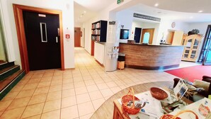 Un área de recepción con mostrador, televisor, estantería y un cubo de basura.