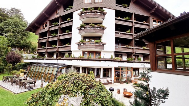 Un hotel de varios pisos con balcones, mobiliario exterior y un jardín.