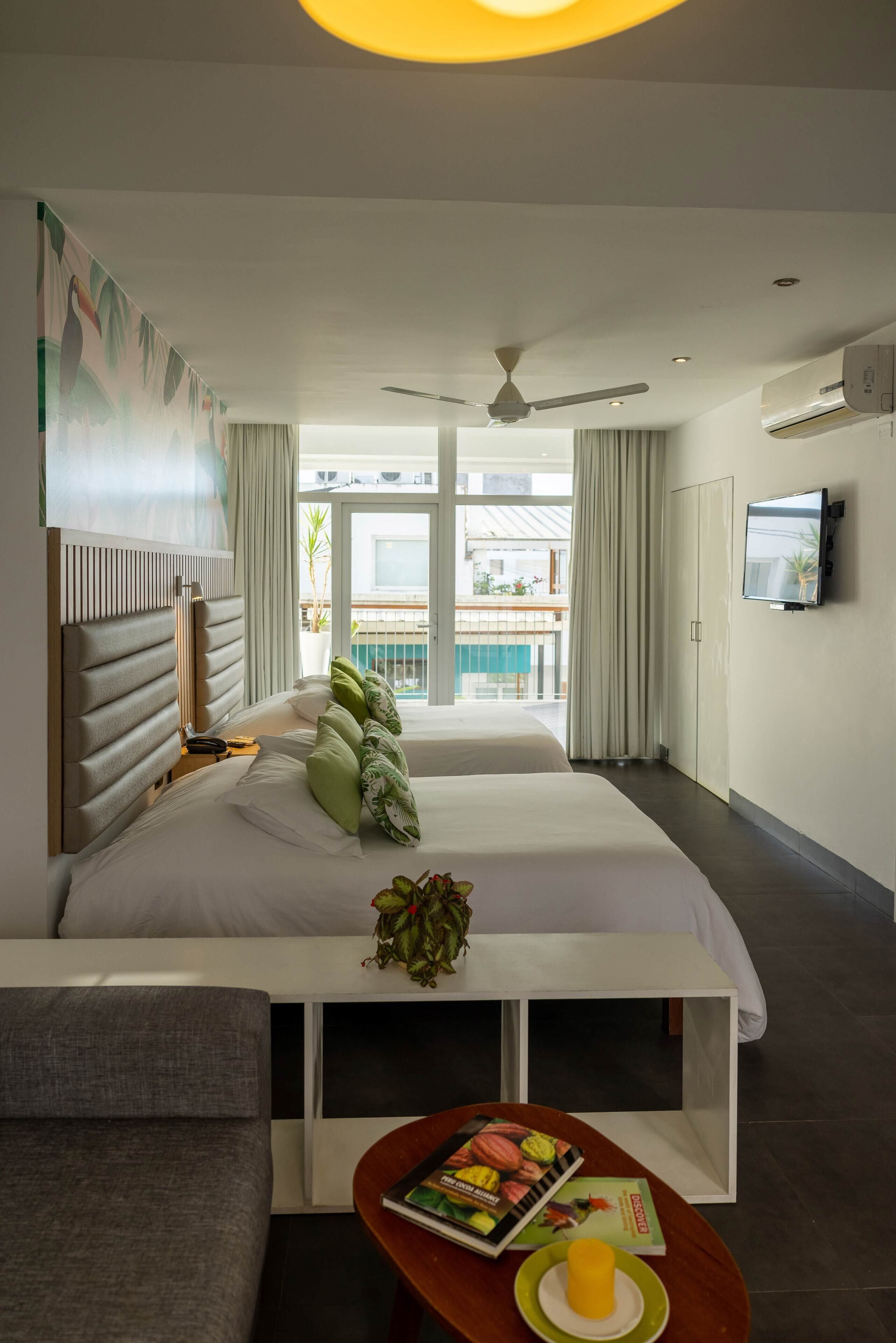 A hotel room with two beds, a sofa, a TV, and a balcony with a pool view.