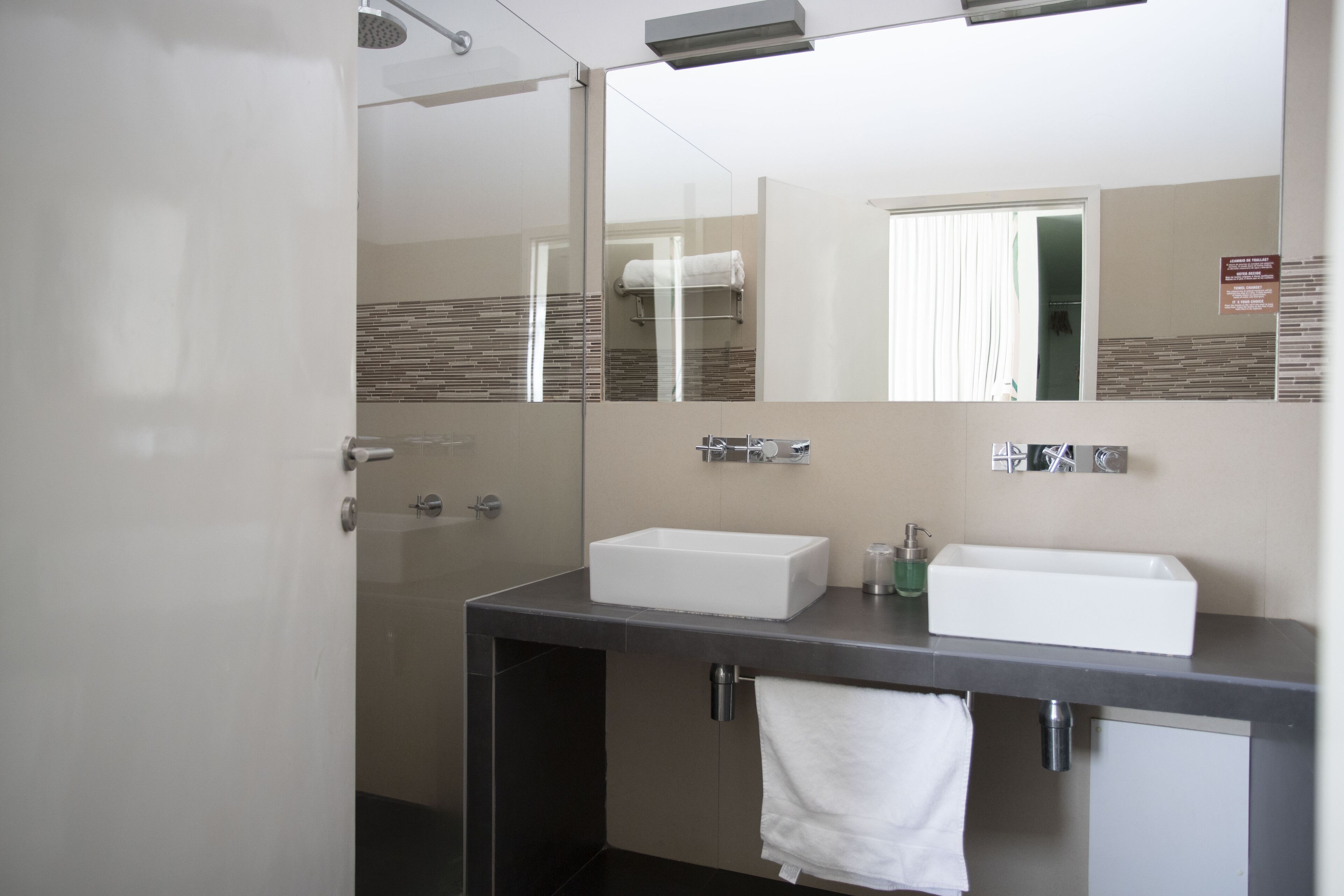 A modern bathroom with a large mirror, two sinks, and a shower.