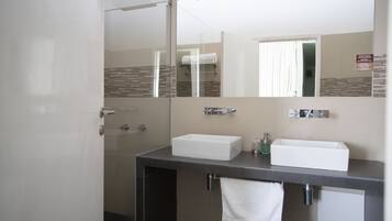 A modern bathroom with a large mirror, two sinks, and a shower.