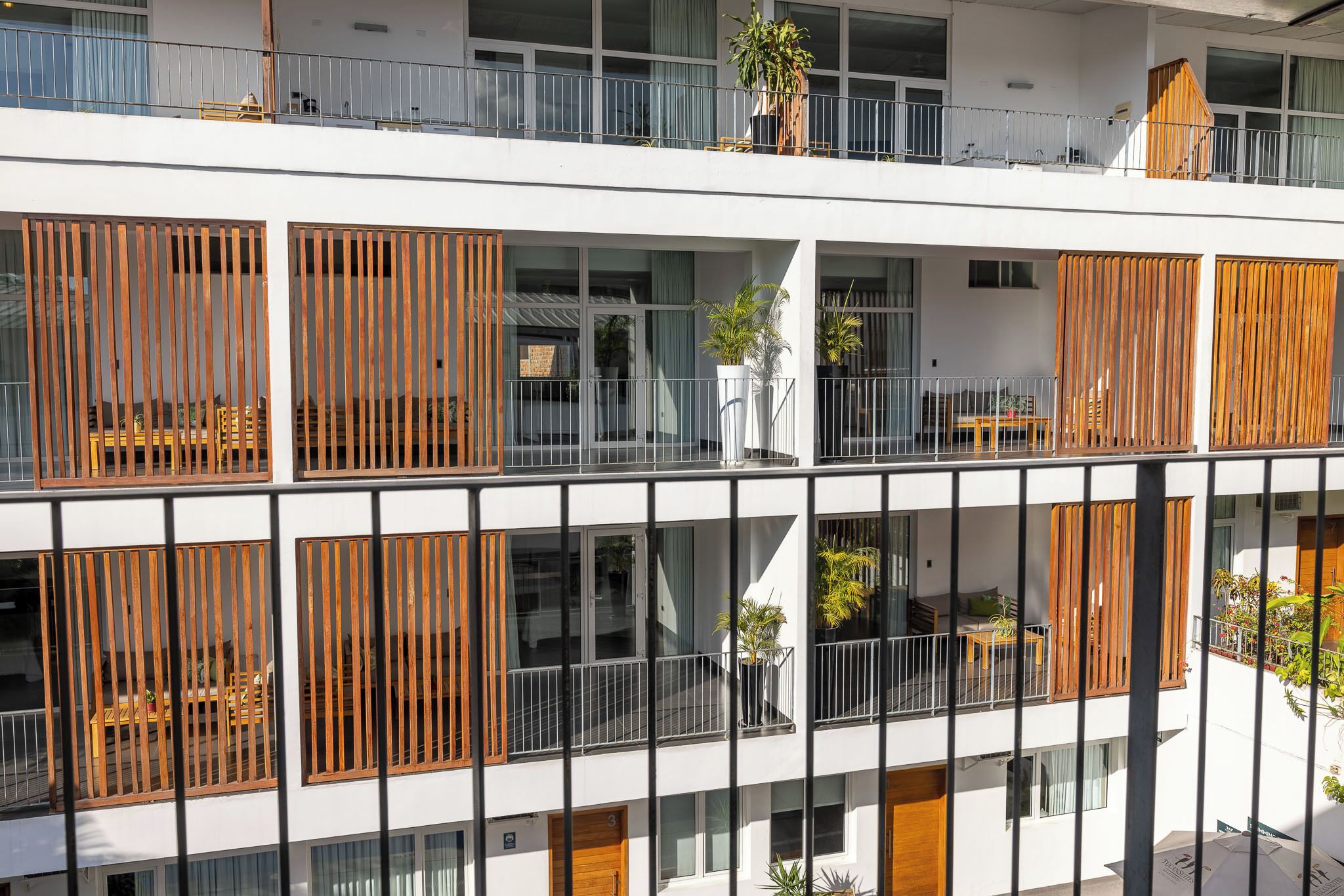 A multi-story building with balconies, wooden slats, and potted plants.