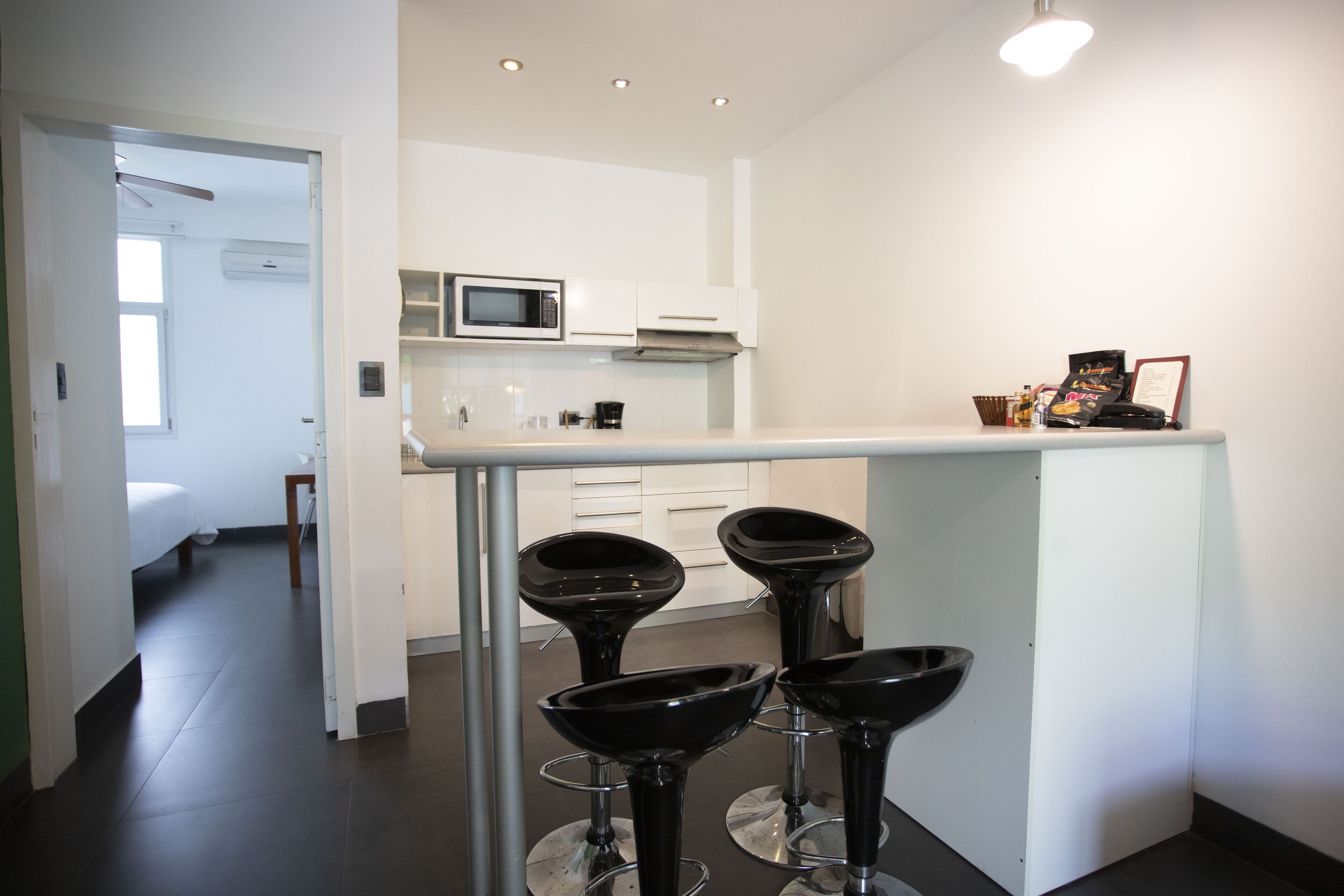Una cocina moderna con armarios blancos, un microondas y una cafetera. Hay tres taburetes negros frente a la encimera.