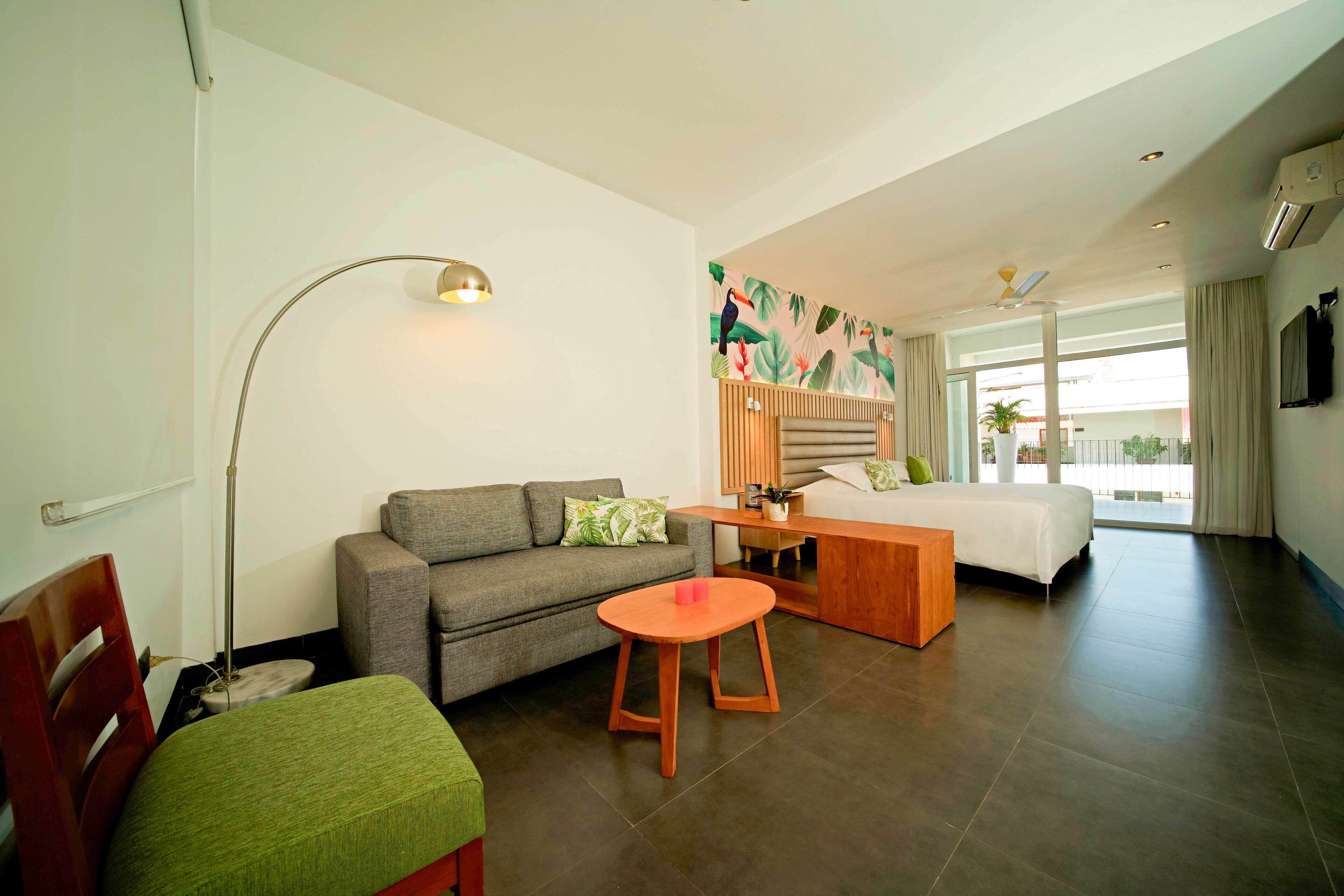 Ein modernes Hotelzimmer mit einer Couch, einem kleinen runden Tisch, einem Bett und einem großen Fenster mit Vorhängen.
