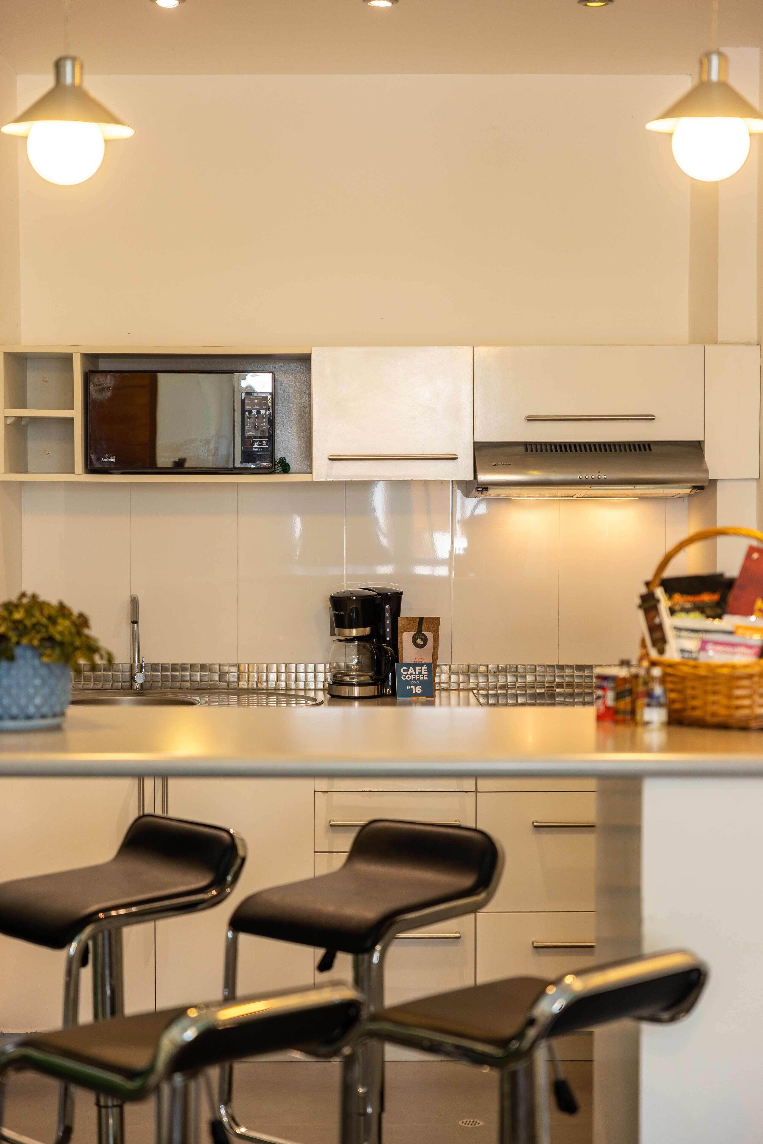 Una cocina moderna con armarios blancos, electrodomésticos de acero inoxidable y una isla central con taburetes de bar.
