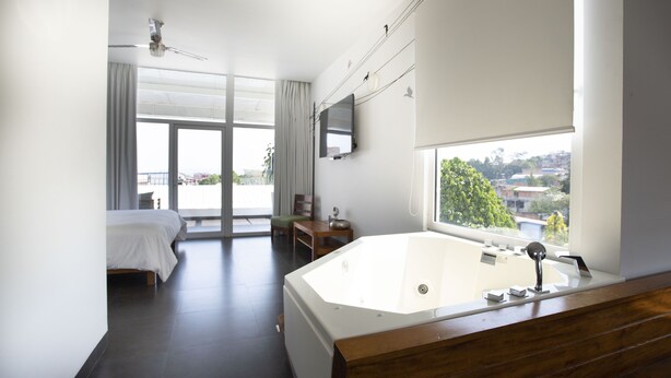 Quarto de hotel moderno com uma banheira grande, uma cama, uma escrivaninha e uma televisão.