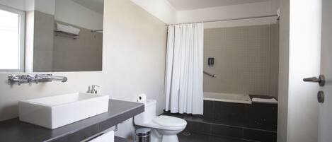 A modern bathroom with a large mirror, a white sink, a toilet, and a shower area.
