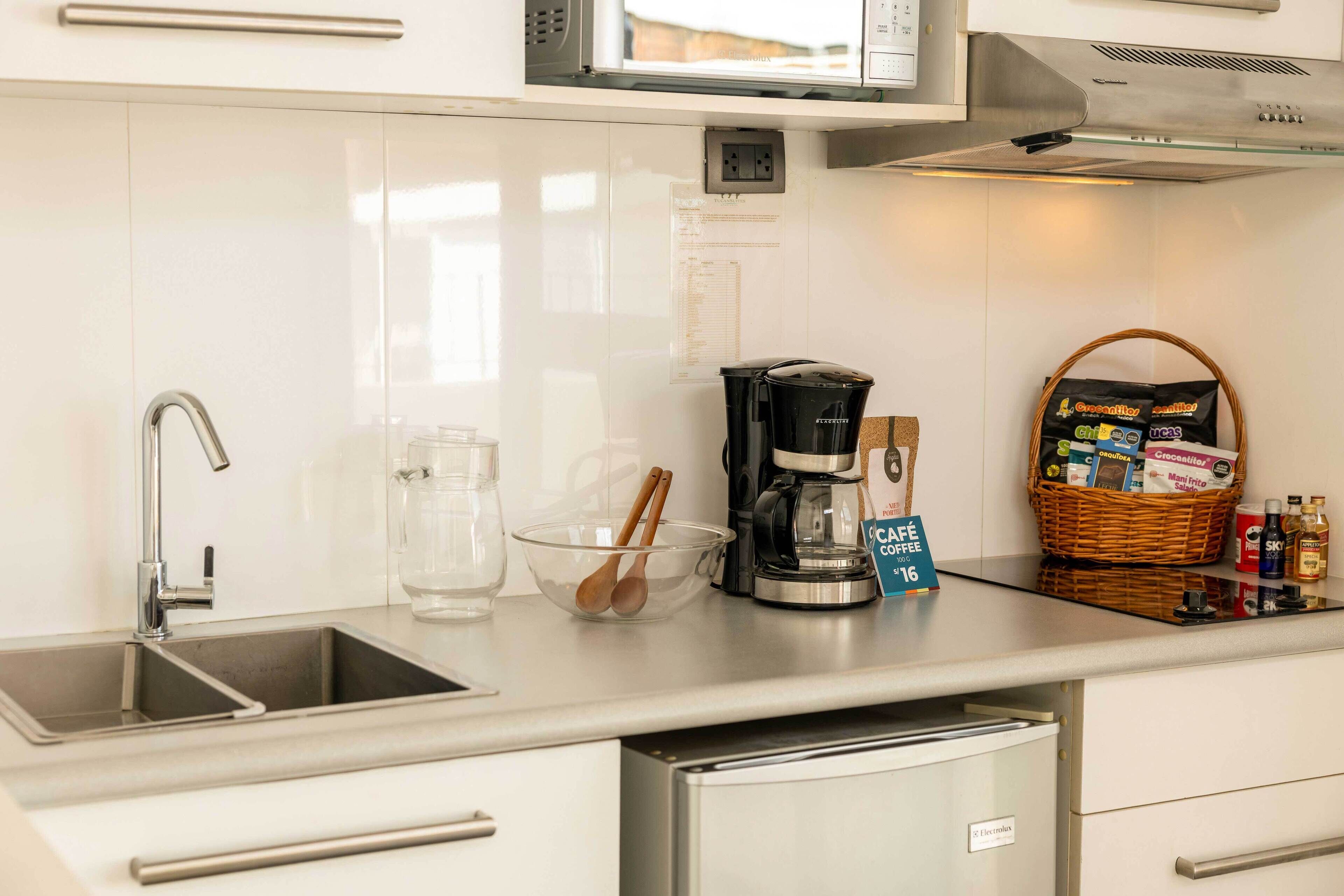 Una cucina moderna con lavello in acciaio inossidabile, una macchina per il caffè, una ciotola di vetro con utensili di legno e un cesto di snack.