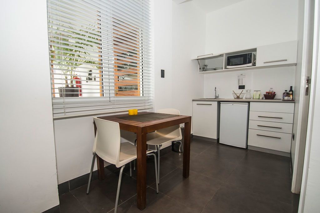 A compact kitchen with white cabinets, a microwave, and a small dining area with a wooden table and two chairs.