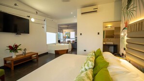 Quarto de hotel moderno com uma cama grande, uma TV de tela plana na parede, um banco de madeira e uma mesinha com um vaso de flores.