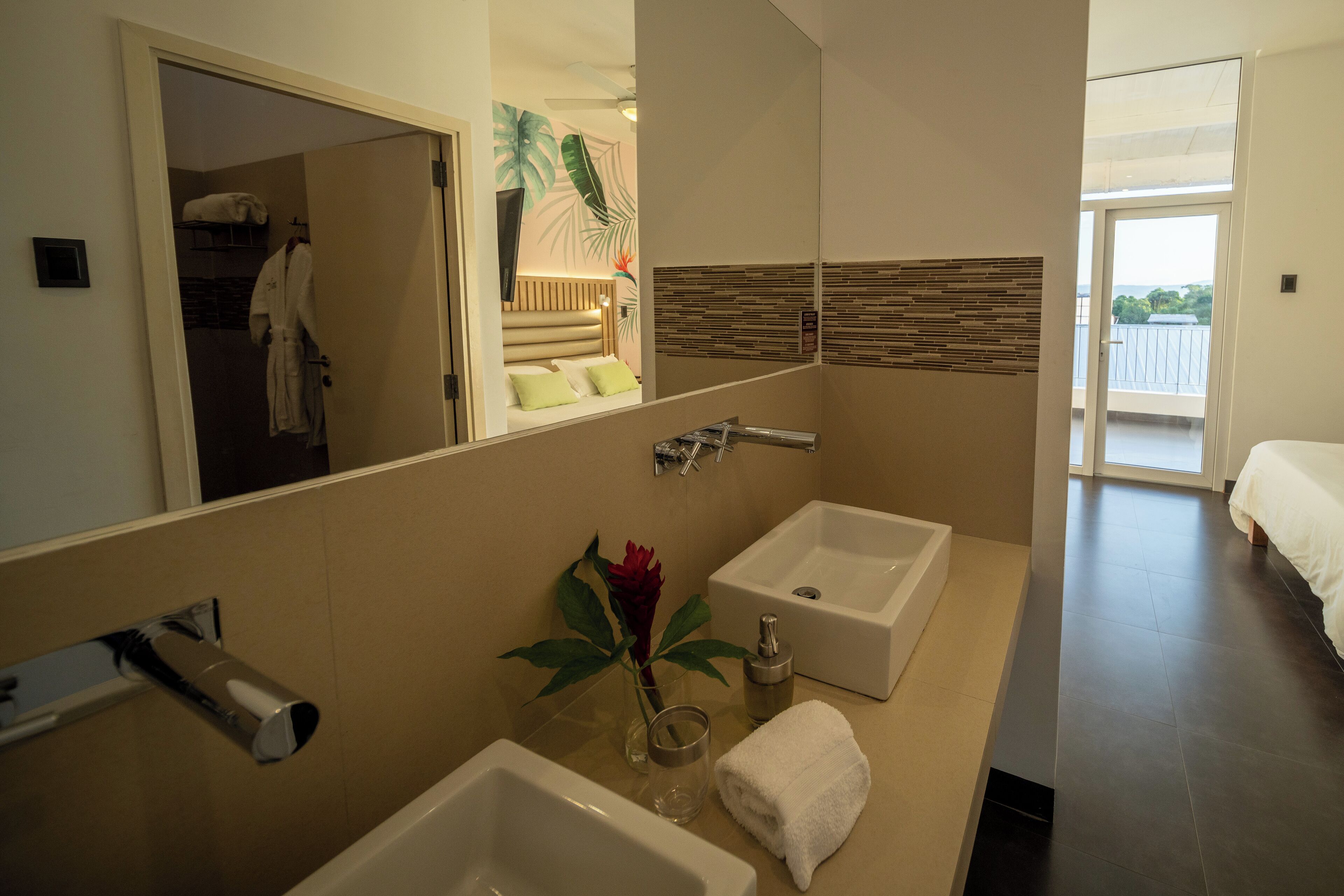 A modern bathroom with a large mirror, two sinks, a shower, and a visible balcony.