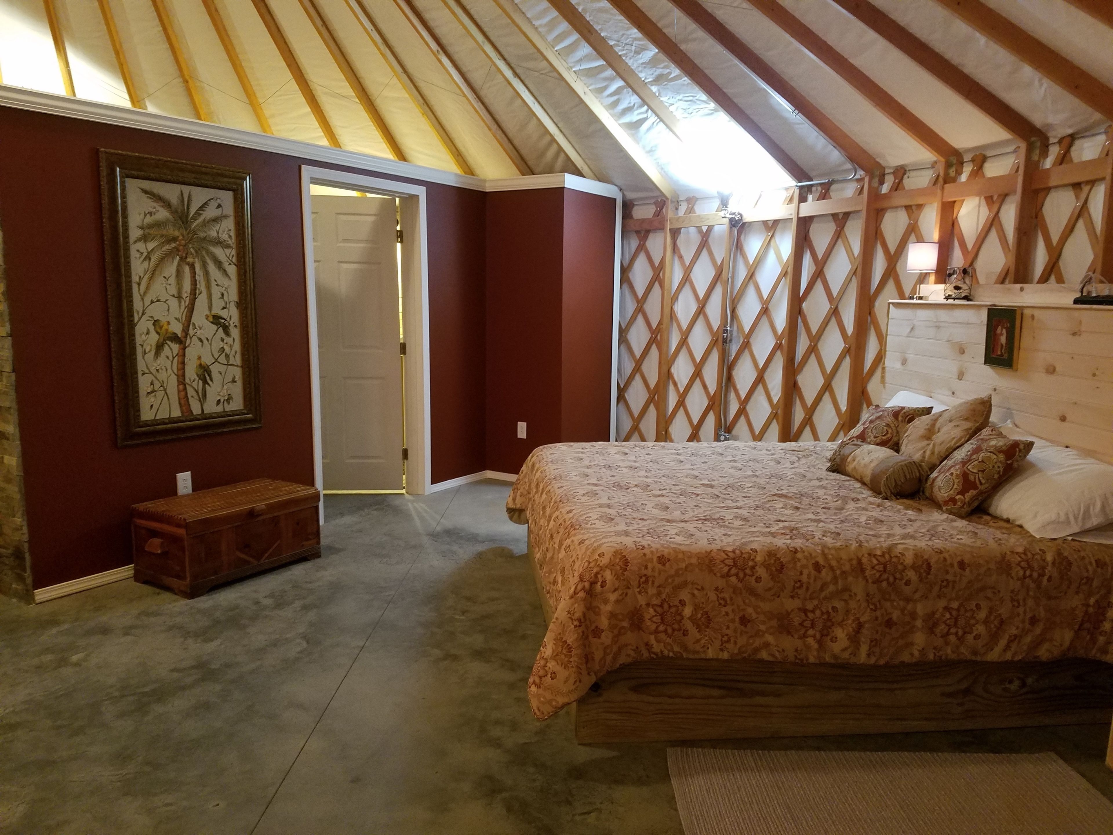Un dormitorio con una cama, un banco de madera, una puerta y un muro con celosía.