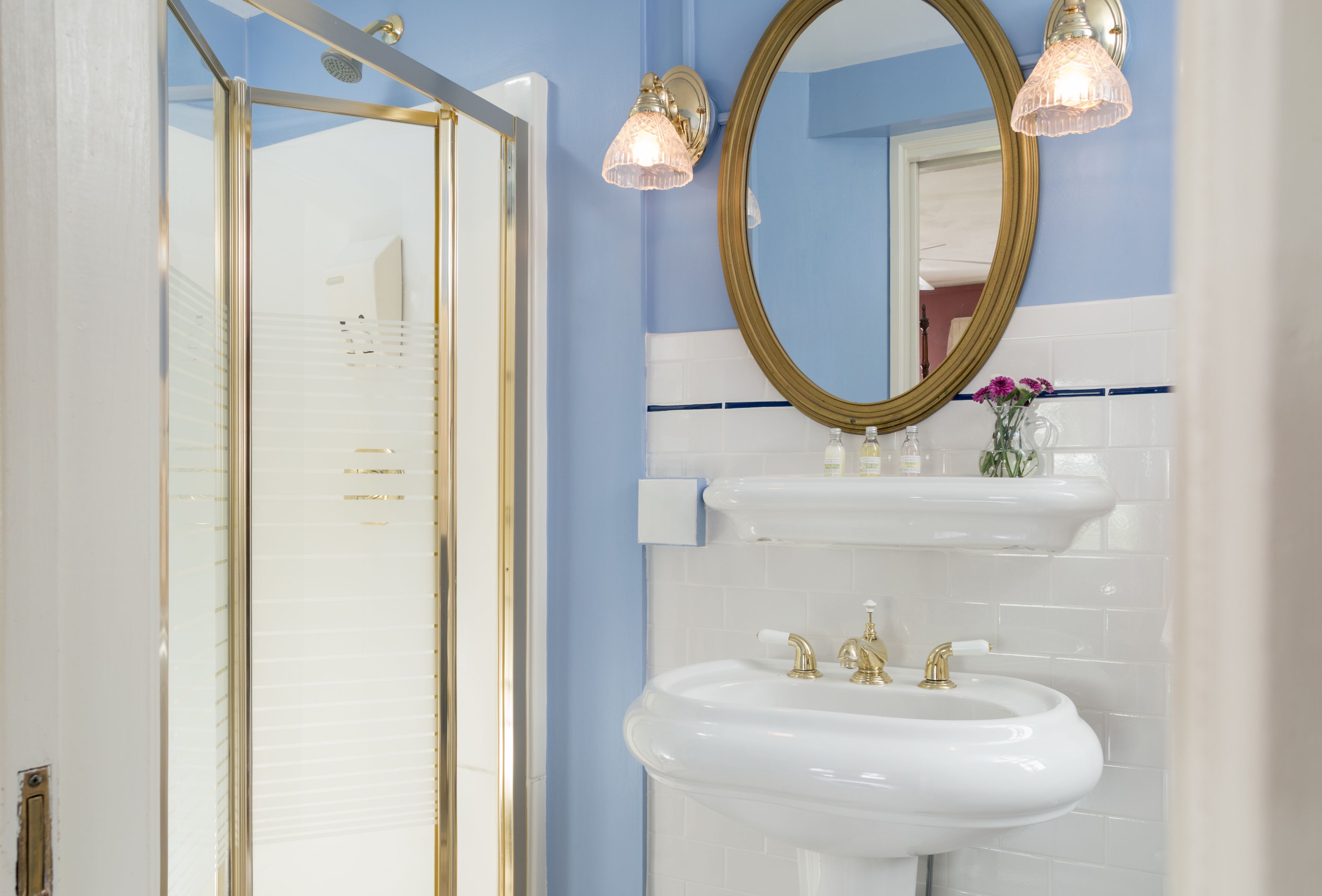 A bathroom with a glass shower enclosure, a double sink with gold fixtures, and a large mirror with a gold frame.