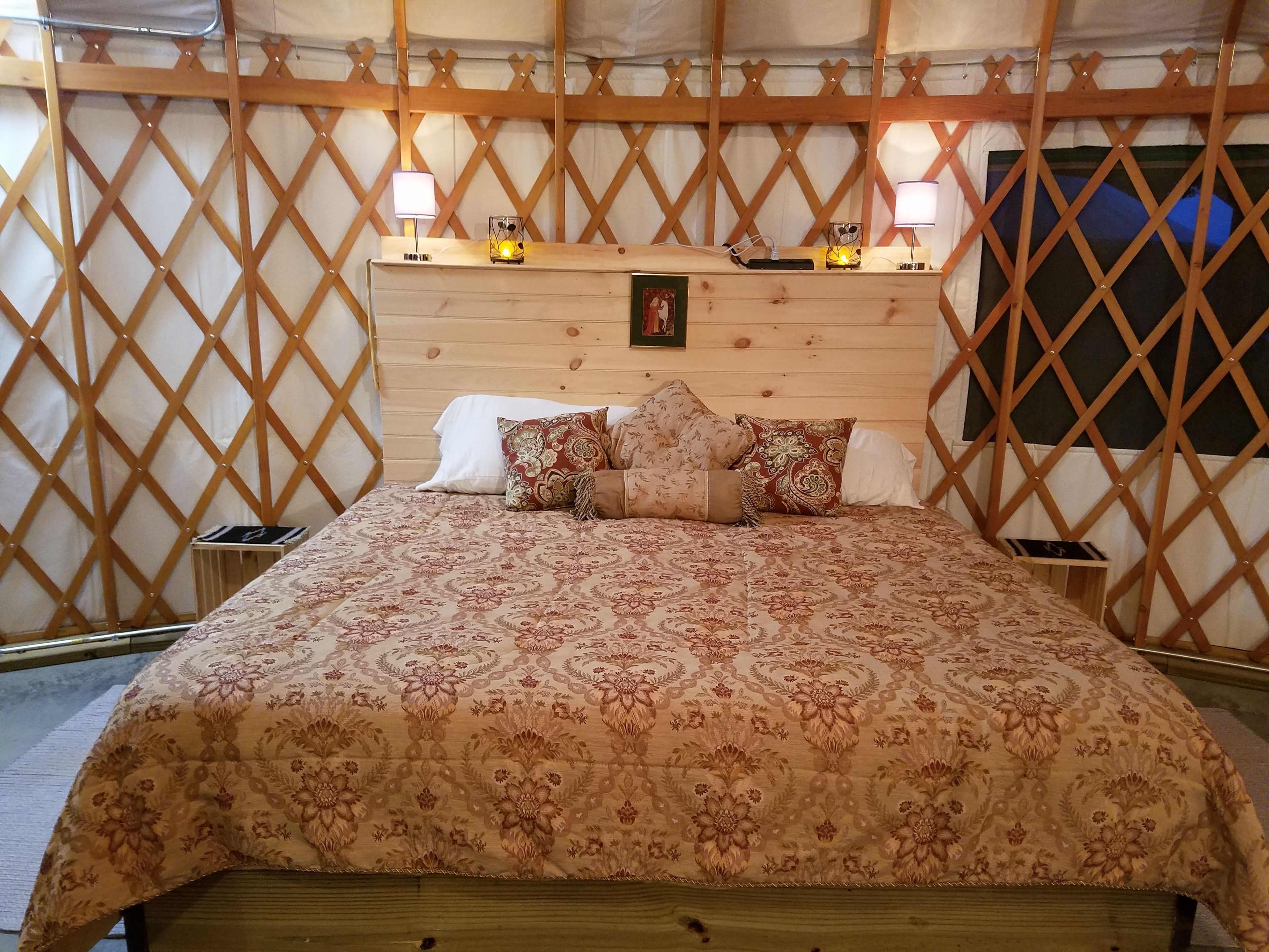 A bed with a floral-patterned bedspread, a wooden headboard, and two bedside lamps.